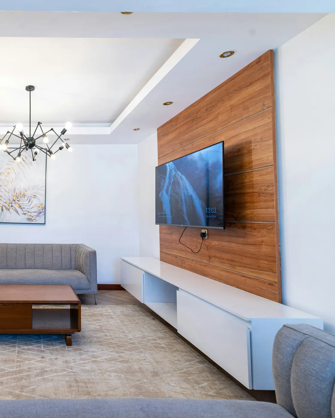 Grand séjour blanc avec mur télé en bois, canapé gris et coin repas