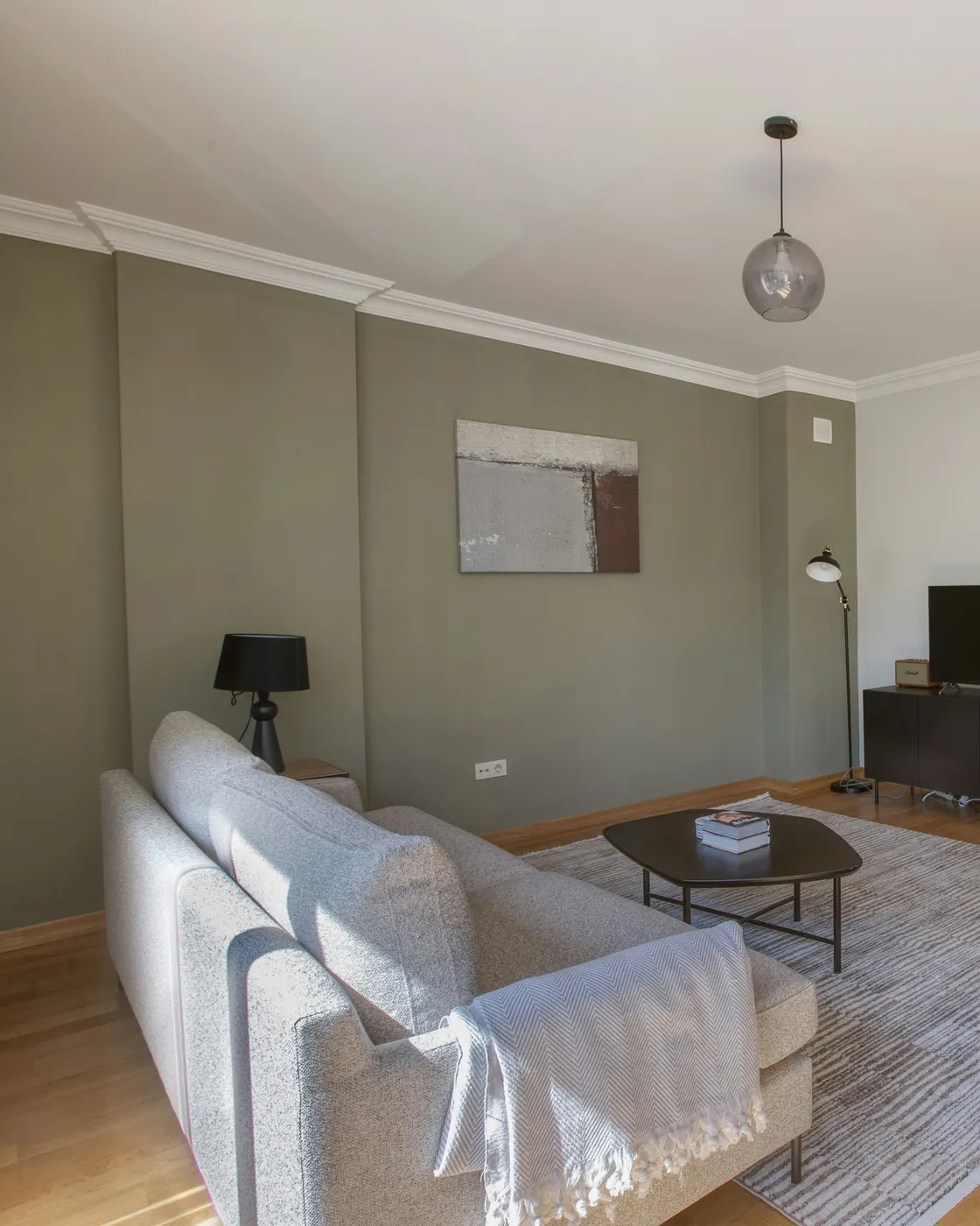 Salon lumineux aux murs vert sauge avec canapé gris et parquet en chêne